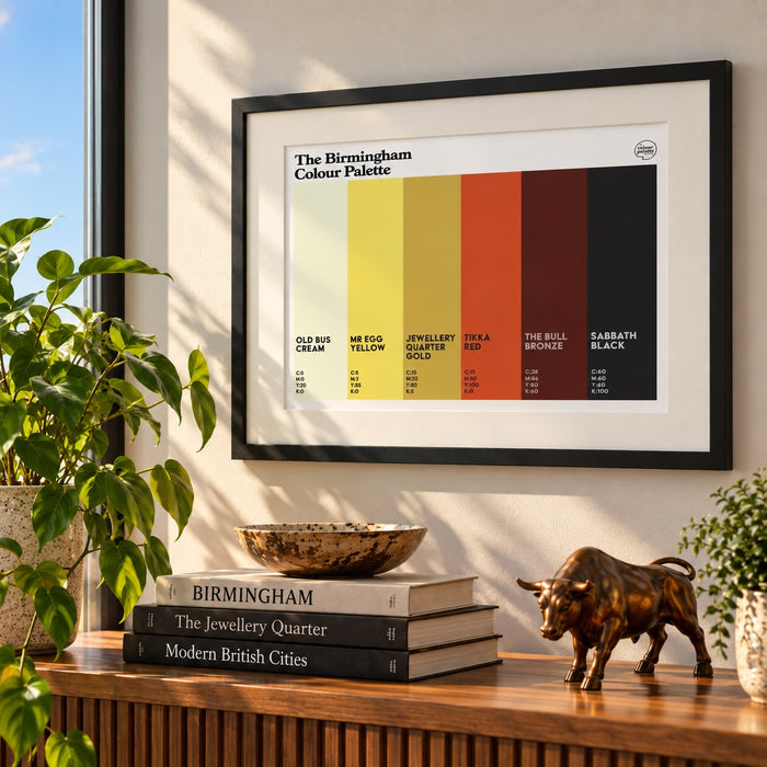 A framed 'The Birmingham Colour Palette' art print hangs on a light wall above a wooden console table. The print features six color blocks in cream, yellow, orange, red, brown, and black, labeled with text and color codes.