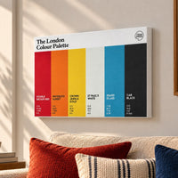 A canvas poster titled 'The London Colour Palette' hangs on a beige wall above a sofa with red, cream, and blue pillows. The poster features six vertical color blocks in red, orange, yellow, blue, black, and gray with London color names and hex codes.